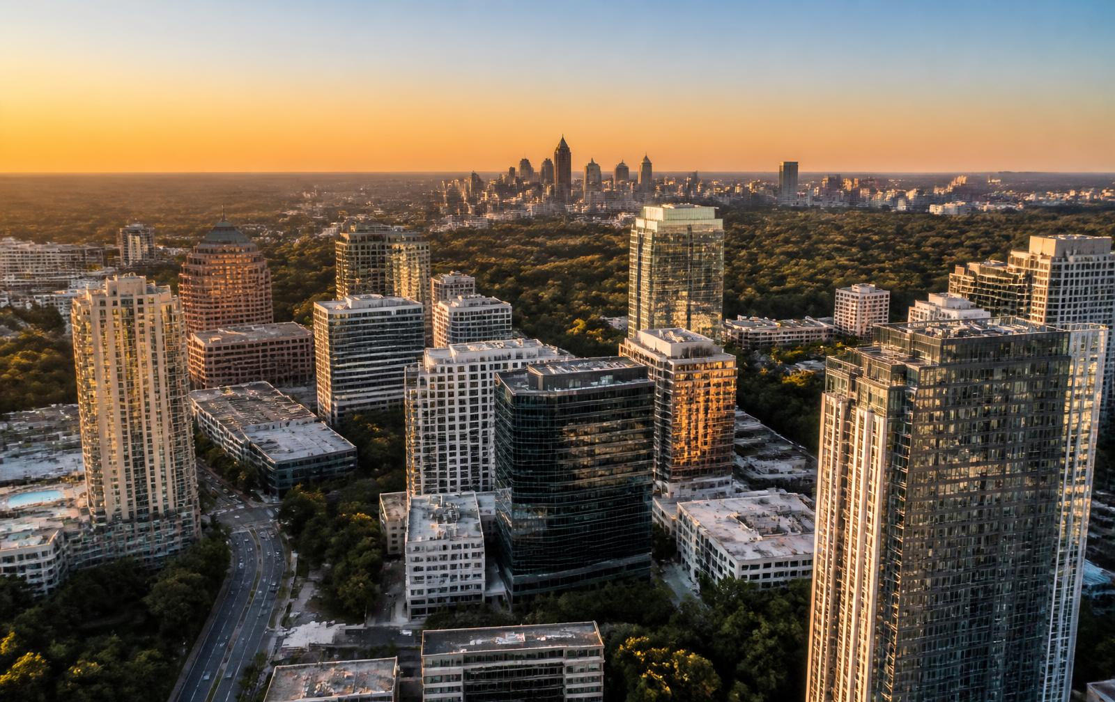 Aerial view of Buckhead and Midtown Atlanta, Georgia, with hotel and office towers above the city's tree canopy at golden hour.