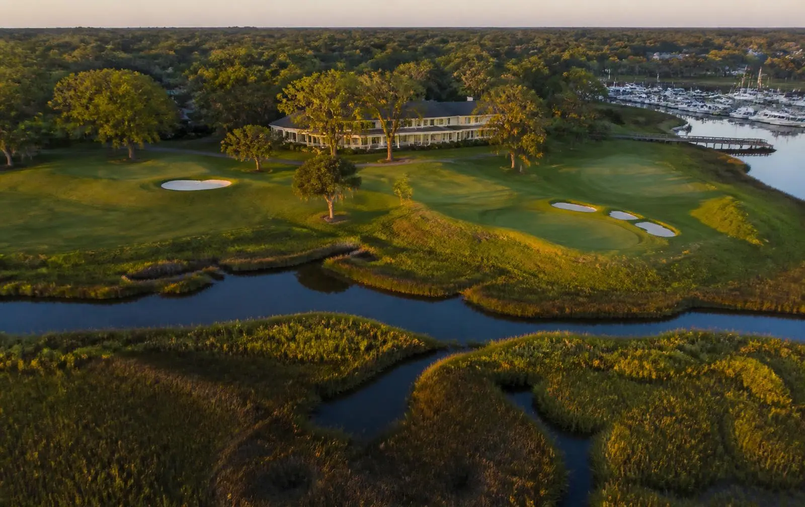 Aerial view of a South Carolina Lowcountry golf club beside tidal marsh creeks near Hilton Head at golden hour.