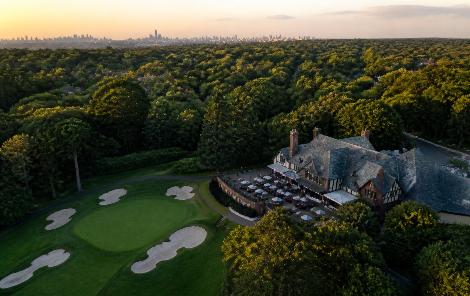 Aerial view of a century-old private country club in northern New Jersey at golden hour, with the Manhattan skyline on the horizon.
